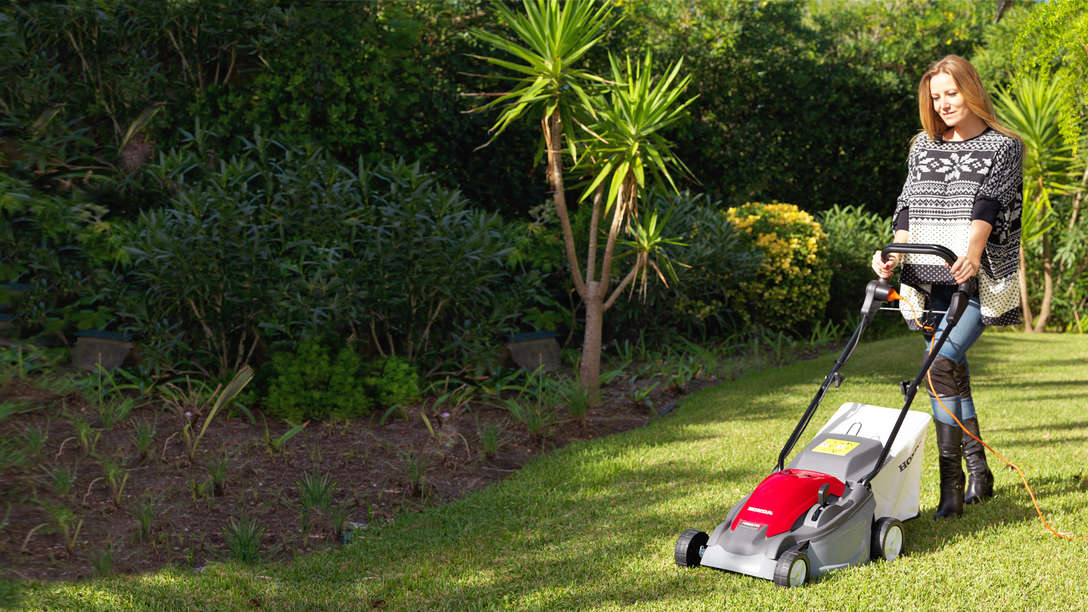Honda HRE-Rasenmäher, Dreiviertelfrontansicht, nach links zeigend, Einsatz nach Modell, Gartenumgebung.