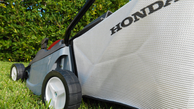 Honda HRE-Rasenmäher, Dreiviertelrückansicht, Nahaufnahme des Grasfangsacks, Gartenumgebung.