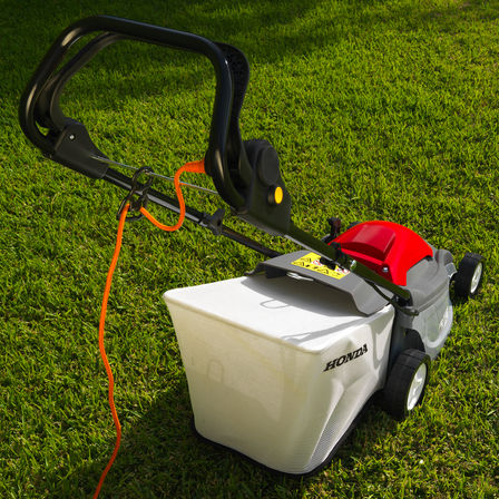 Honda HRE-Rasenmäher, Dreiviertelrückansicht, Kabel im Fokus, Gartenumgebung.