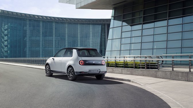 entfernte Rückansicht des weißen Honda E Elektroautos, das vor einem Gebäude geparkt wird