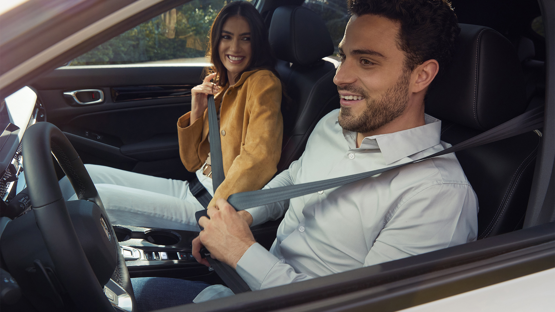 Zwei Personen sitzen vorne in einem Honda Civic Hybrid und legen ihre Sicherheitsgurte an.