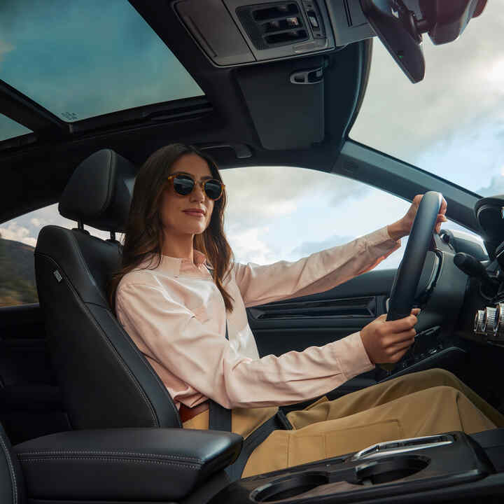 Eine Frau mit Sonnenbrille, die mit den Händen das Lenkrad des Civic Hybrid umfasst