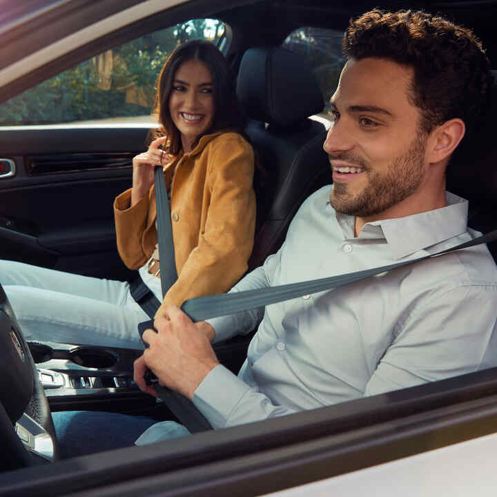 Zwei Personen sitzen vorne in einem Honda Civic Hybrid und legen ihre Sicherheitsgurte an.