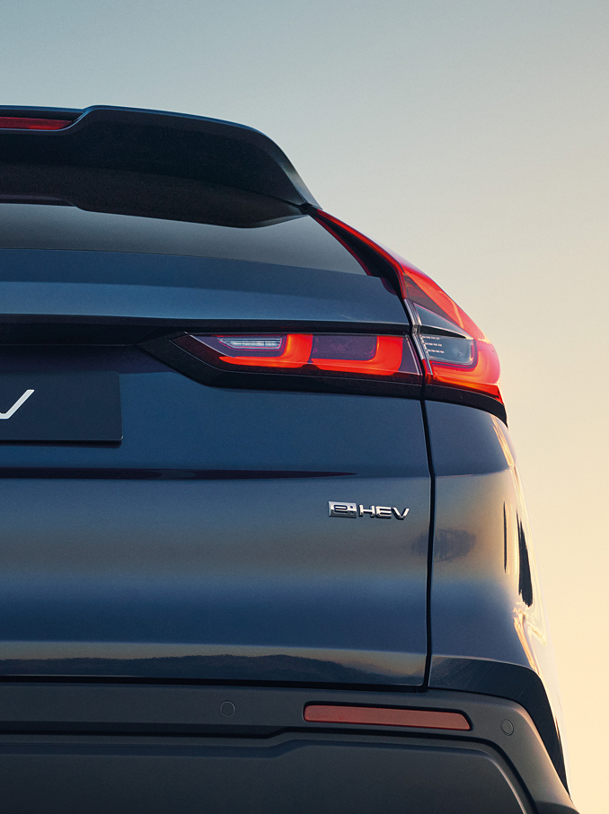 Heckaufnahme eines dunkelblauen Honda CR-V e:HEV mit Honda-Emblem, CR-V-Schriftzug und beleuchteten Signature-LED-Rückleuchten vor einem sanften Sonnenuntergang.