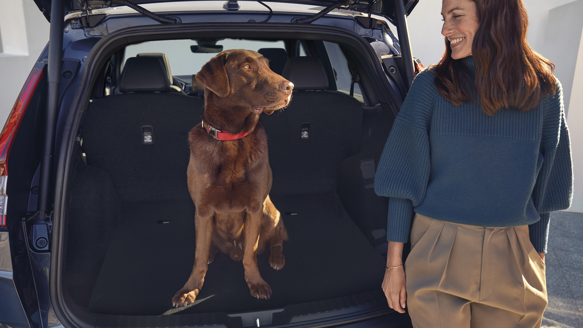 Honda CR-V Hybrid, Heckansicht mit Hund und Model im Kofferraum.