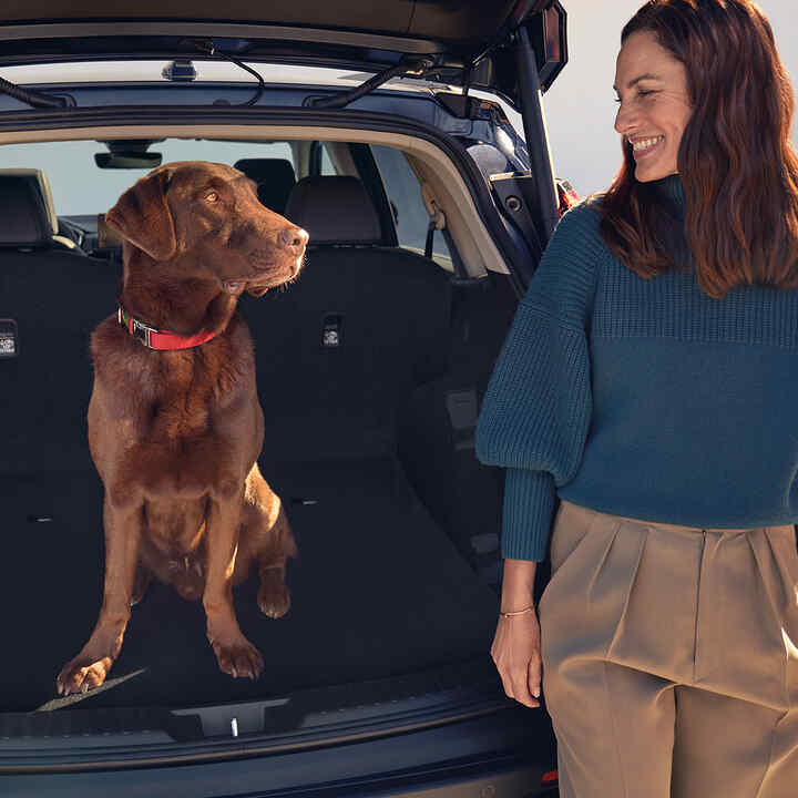 Honda CR-V Hybrid, Heckansicht mit Hund und Model im Kofferraum.
