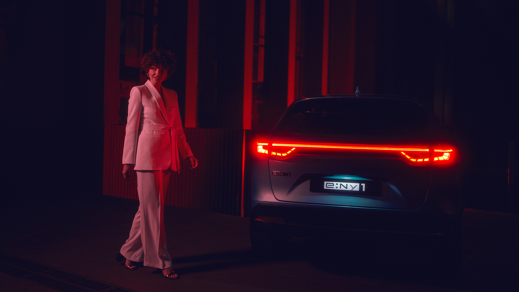 Model neben dem beleuchteten Heck eines Honda e:Ny1 bei Nacht.
