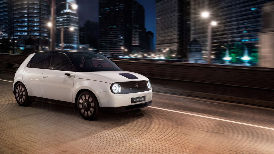 Vorderansicht des weißen Honda e Elektroautos, das nachts durch eine Stadt fährt