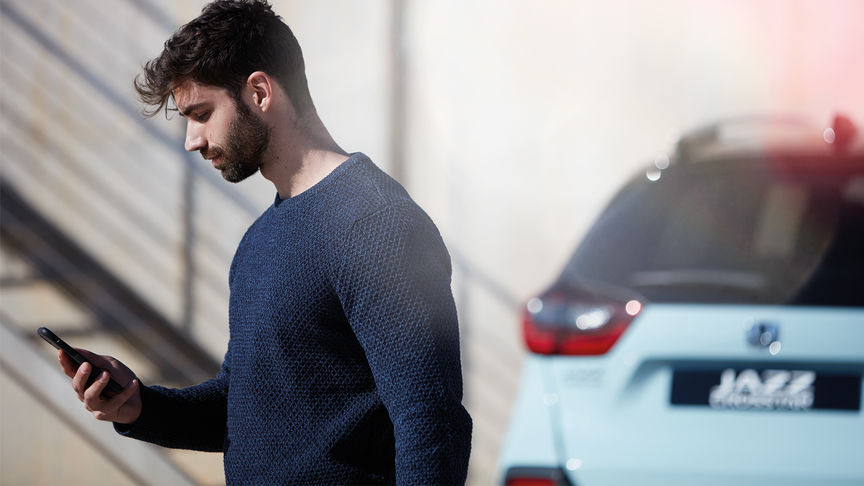 Honda Jazz rear in the background with man using Honda + app away from vehicle