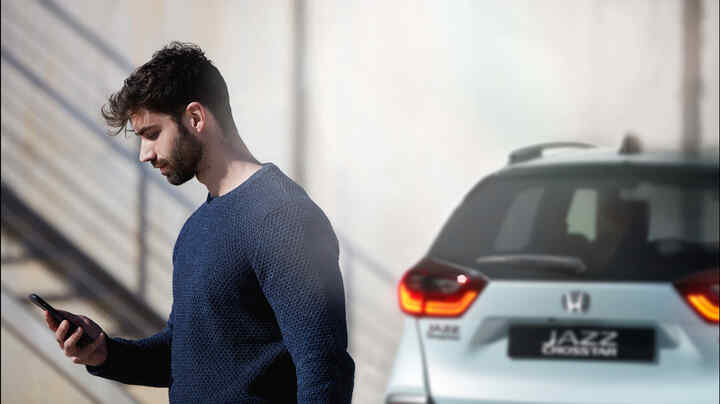 Eine Person, die auf ein Smartphone schaut, mit einem Honda Jazz Crosstar im Hintergrund.