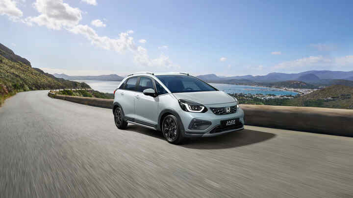 3/4-Frontansicht eines fahrenden Honda Jazz Hybrid mit reizvoller Landschaft im Hintergrund.