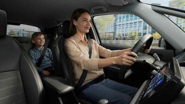 Eine Frau, die einen Honda Jazz Hybrid fährt, mit einem Kind auf dem Rücksitz.