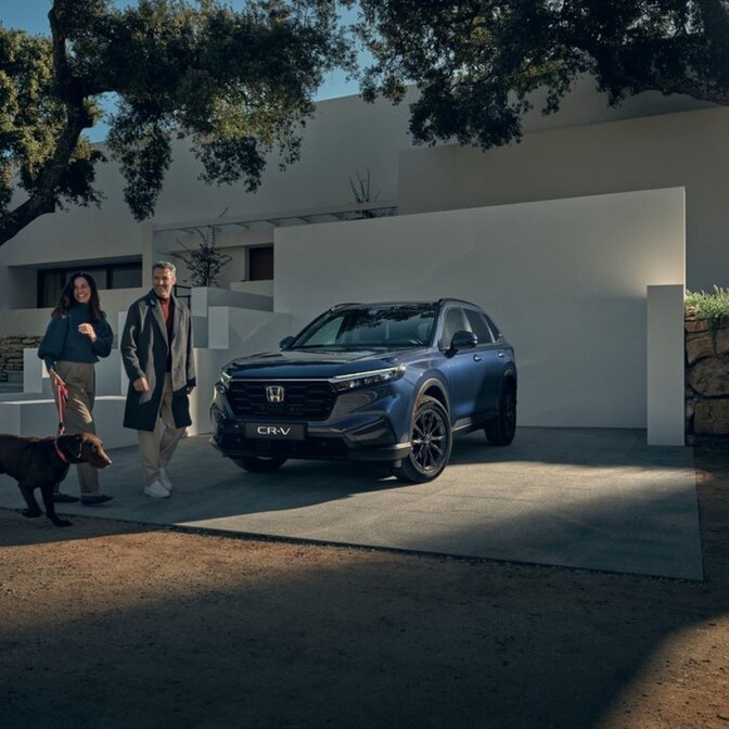 Zwei Personen gehen mit ihrem Hund neben einem geparkten Honda CR-V spazieren.