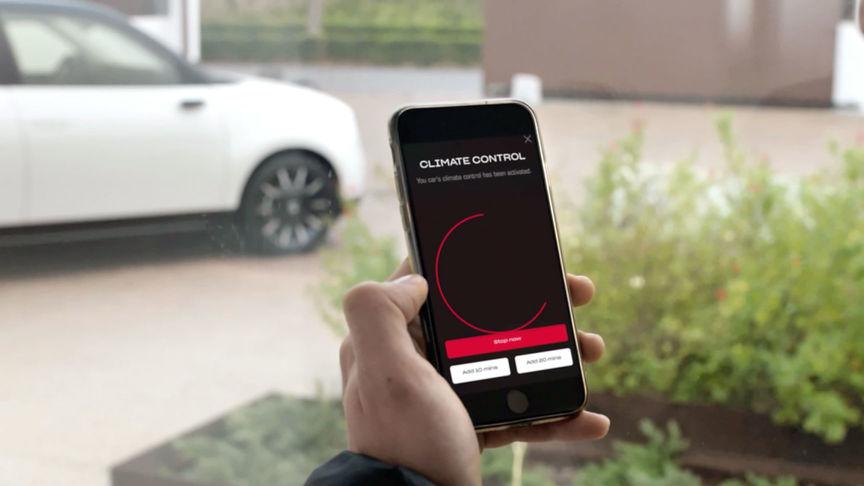 Mann verwendet My Honda Plus App mit einem Honda Jazz Hybrid Crosstar im Hintergrund 