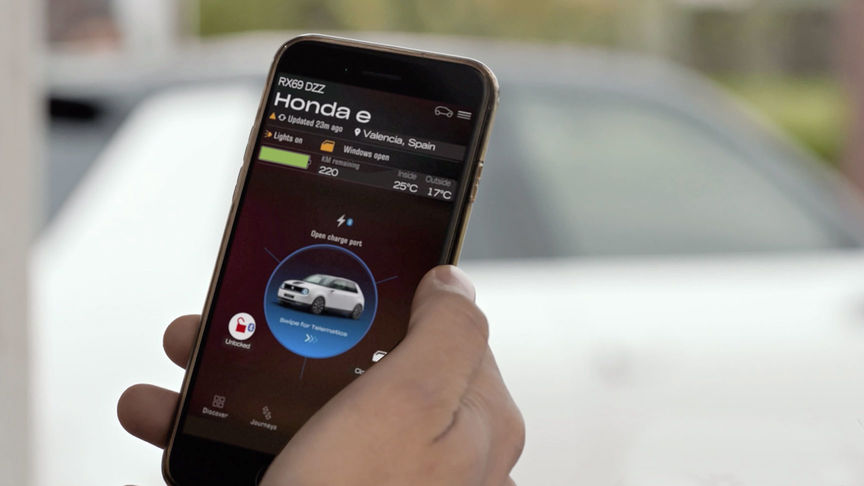 Mann verwendet My Honda Plus App mit einem Honda Jazz Hybrid Crosstar im Hintergrund 