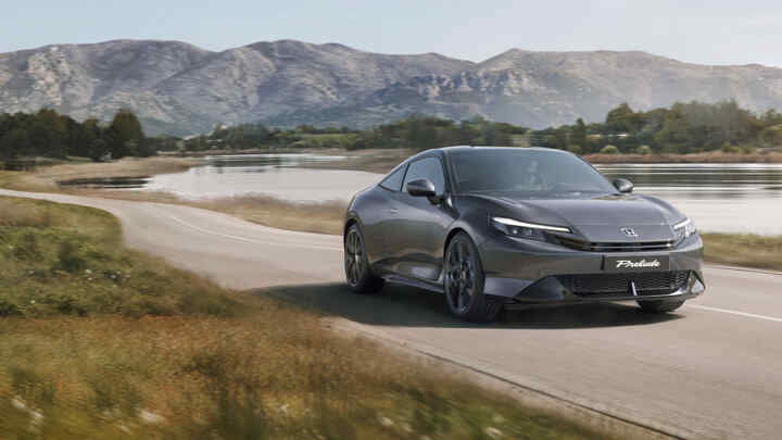 Seitenprofil eines Honda Prelude Hybrid, der an einem See mit grünen Bäumen entlangfährt.