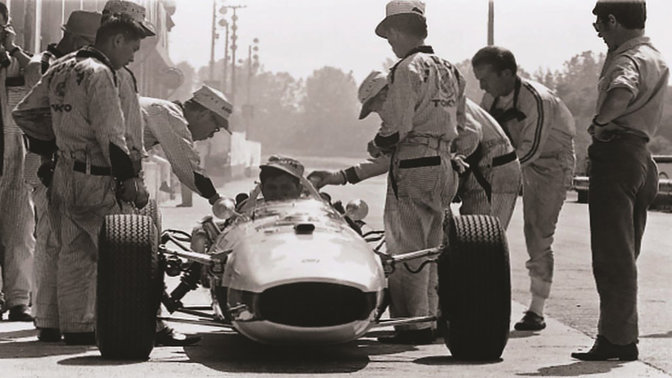 Frontansicht eines Honda Formel-1-Fahrzeugs aus den 1960er Jahren mit Rennfahrer und Ingenieuren.