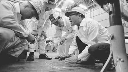 Soichiro Honda und einige Fabrikarbeiter in weißen Overalls.