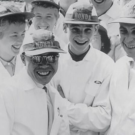 Soichiro Honda und einige Fabrikarbeiter in weißen Overalls.