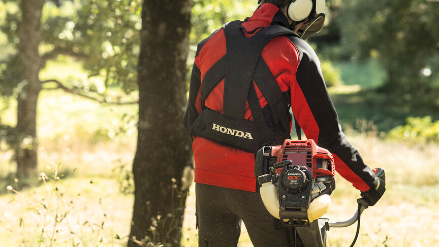 Model mit rückentragbarem Freischneider im Wald.