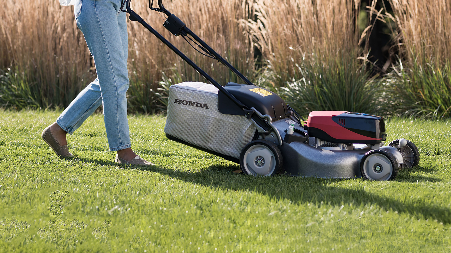Frau beim Schieben eines IZY-ON-Rasenmähers auf dem Rasen.