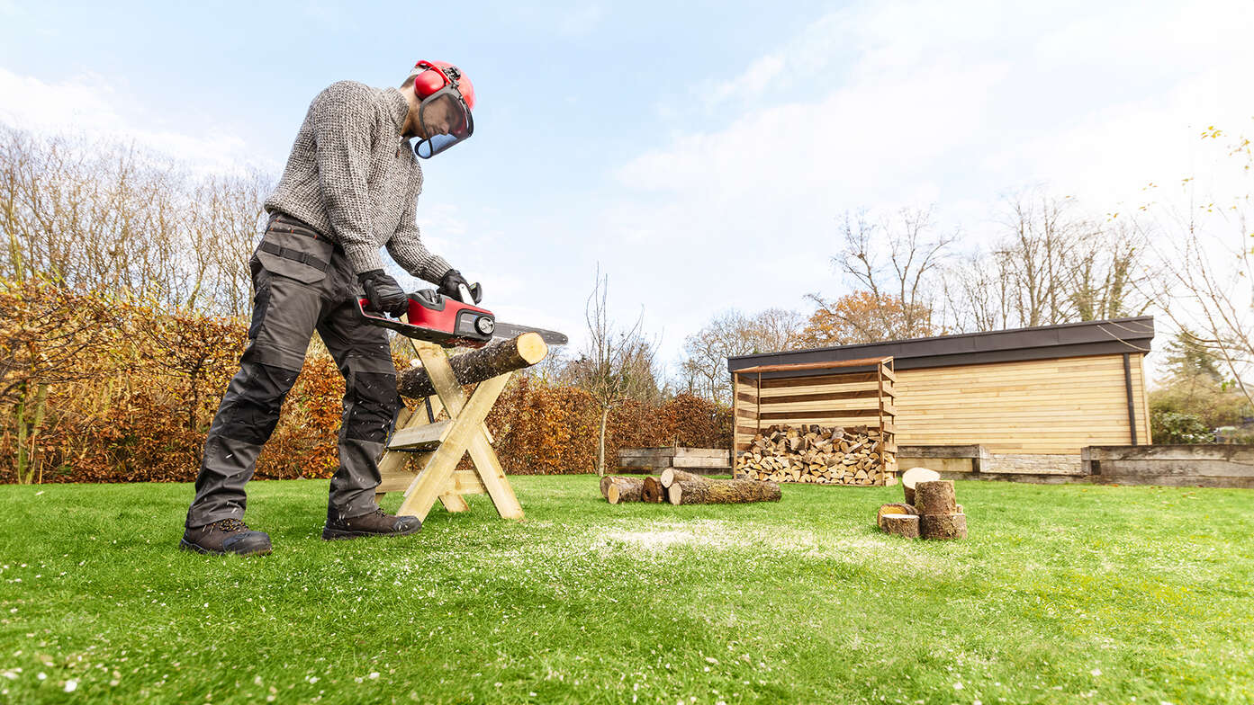 Ein Mann benutzt eine Akku-Kettensäge in einem Garten.