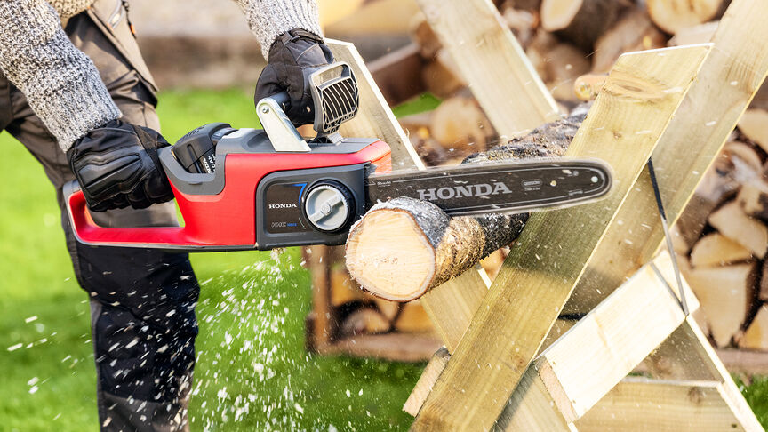 Model beim Holzschneiden mit einer Honda Akku-Kettensäge, Nahaufnahme.