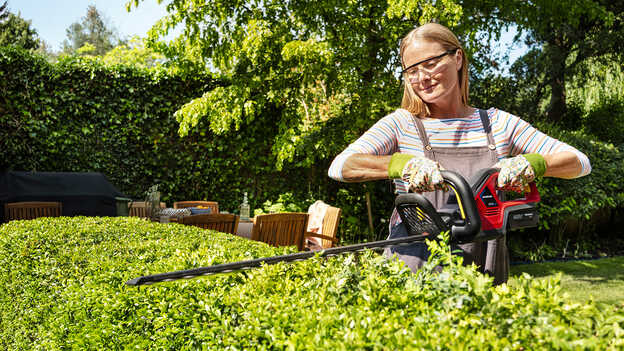 Frau beim Schneiden einer Hecke mit einer Honda Akku-Heckenschere in einem Garten.