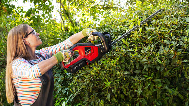 Frau beim Schneiden eines Buschs mit einer Honda Akku-Heckenschere in einem Garten.