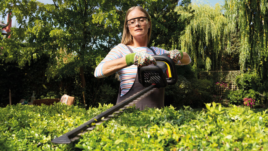 Frau mit Honda Akku-Heckenschere beim Trimmen einer Hecke im Garten.