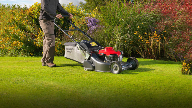 Mann mit Honda HRH Rasenmäher beim Rasenmähen in einem Garten