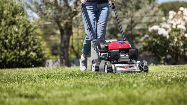 Seitenansicht: Frau mit Honda IZY-Rasenmäher in einem Garten