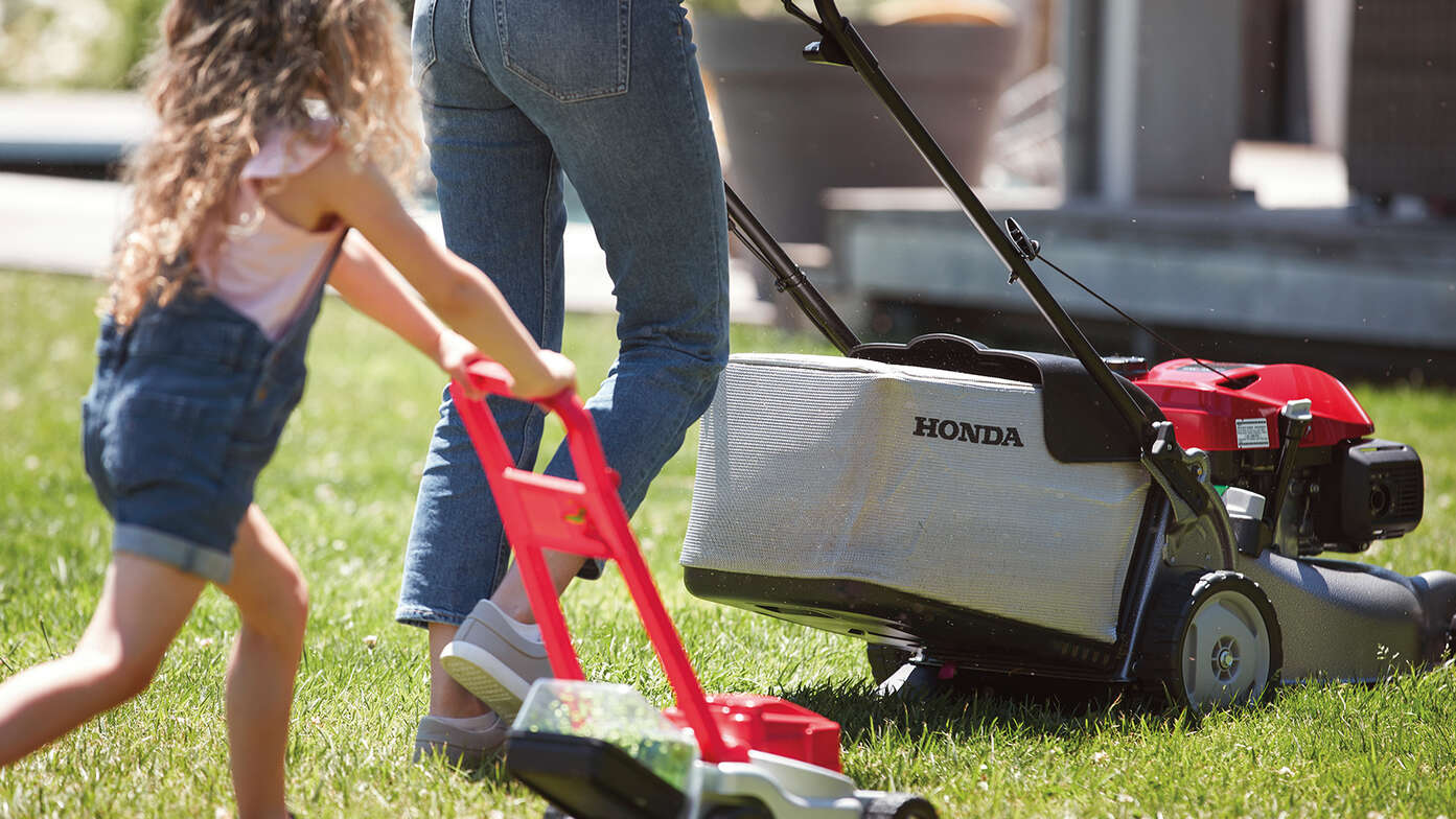 Seitenansicht: Frau und Kind mit Honda IZY-Rasenmäher in einem Garten