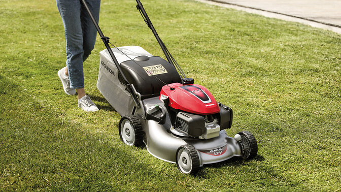 Frau mit Honda IZY Rasenmäher beim Rasenmähen in einem Garten