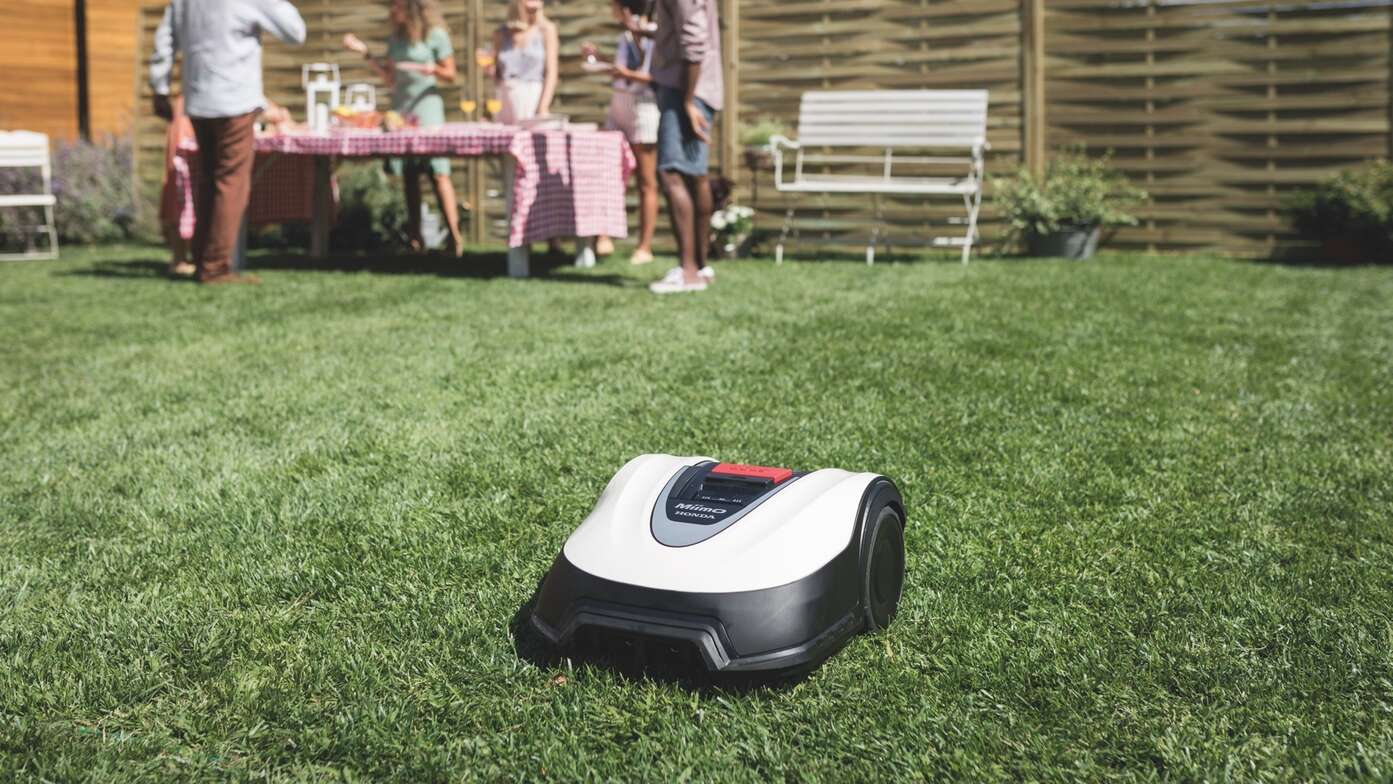 Dreiviertelfrontansicht eines Honda Miimo in einem Garten, im Hintergrund befinden sich Personen und Möbel.