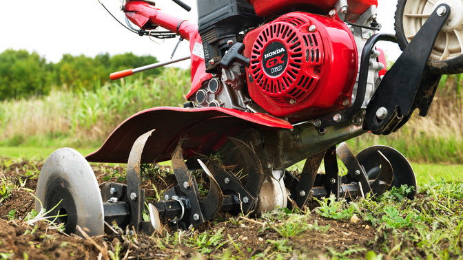 Nahaufnahme der Kompakt-Motorhacke, Fokus auf dem Motor, Gartenumgebung.