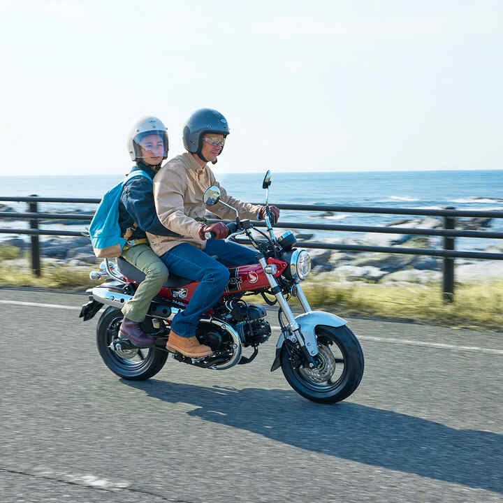 Honda Dax 125 auf einer Küstenstraße mit Fahrer und Sozius