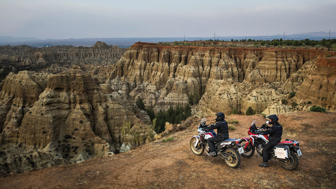 2 Honda Africa Twins mit Fahrern vor einem Canyon.