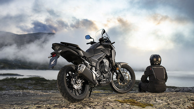 CB500X, 3/4-Heckansicht rechts, neben einem sitzenden Fahrer, Berglandschaft