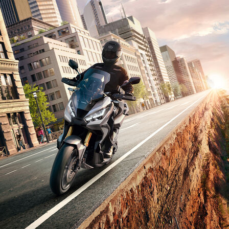 Honda X-ADV – 3/4-Frontansicht, mit Fahrer, zwischen Stadt und Wald, grauer Roller