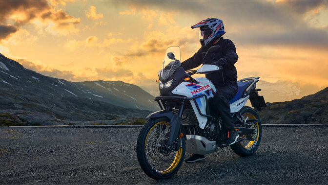 Das Model fährt ein XL750 Transalp Motorrad auf der Straße in den Bergen.