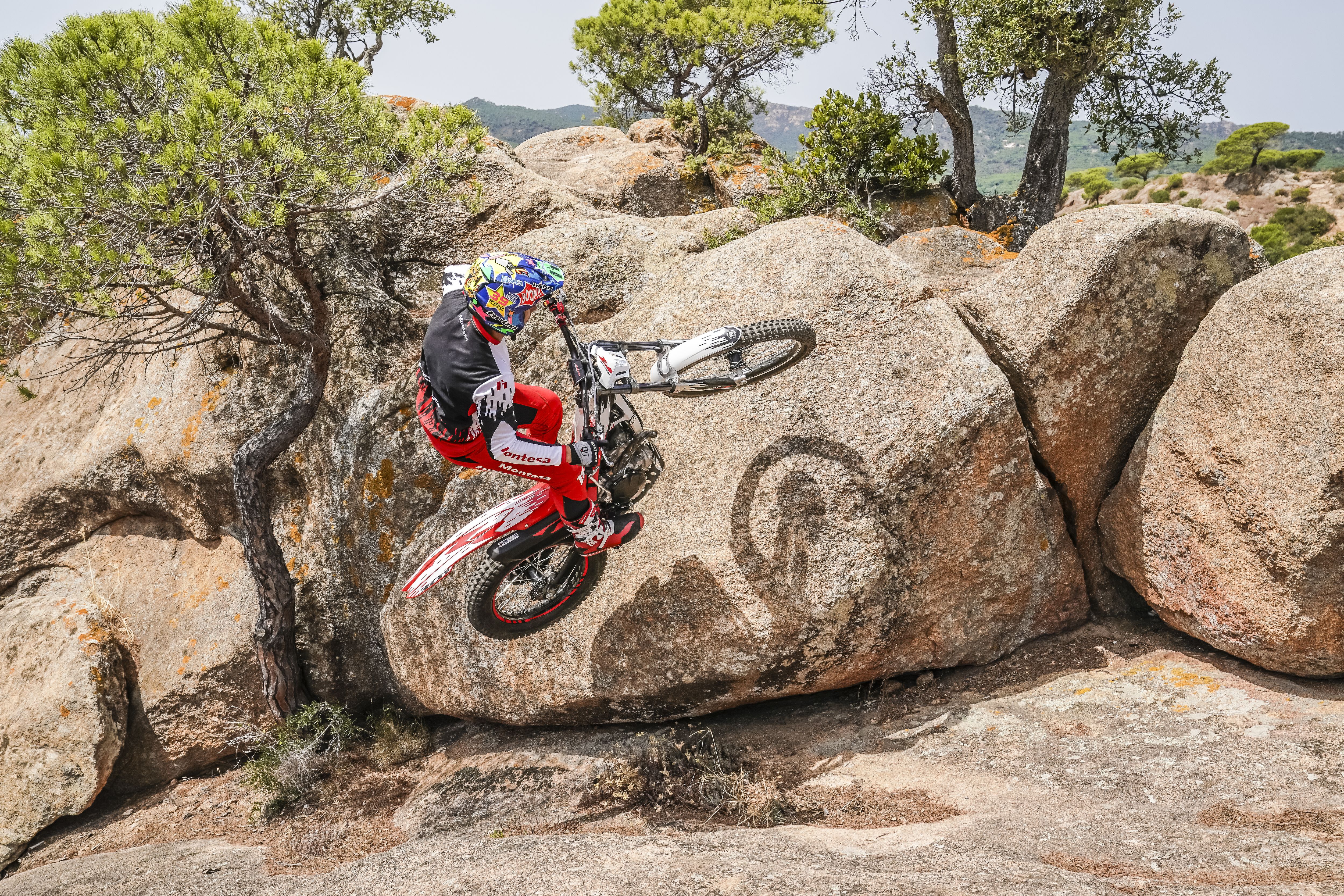 Motorradfahrer macht einen Wheelie auf einer Montesa Cota 301RR auf einer Felsformation.