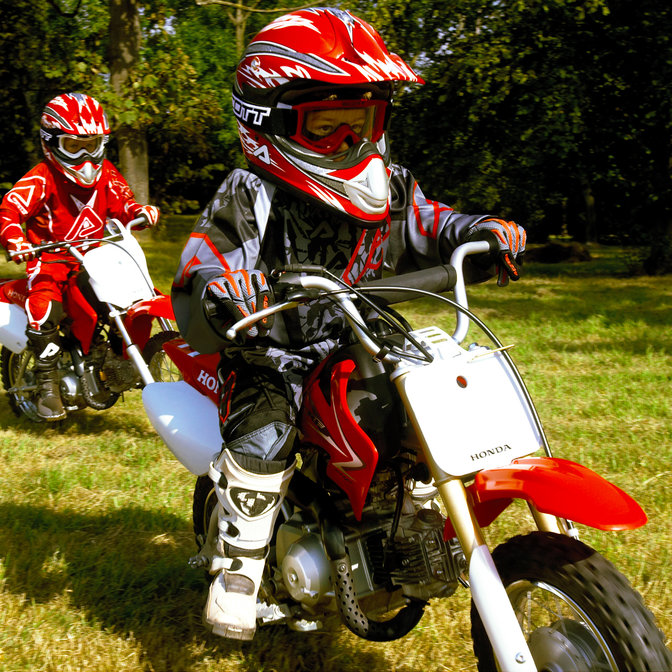 3/4-Seitenansicht zweier CRF50F-Minibikes mit Fahrern auf einer Rasenrennstrecke. Nach rechts weisend.