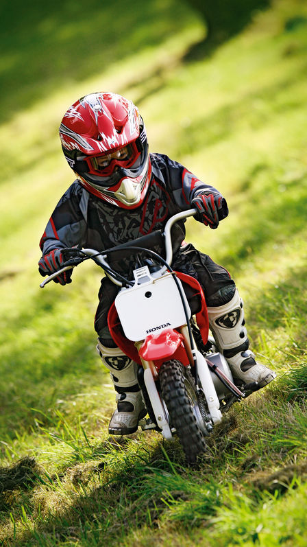 Frontansicht einer CRF50F mit Fahrer an einem Grashang.