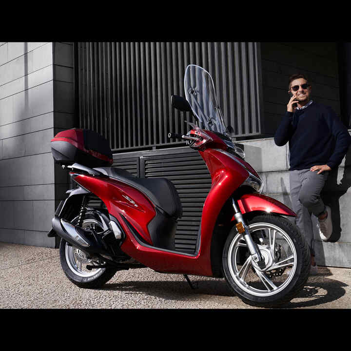 Mann mit Telefon neben einem Honda Roller.