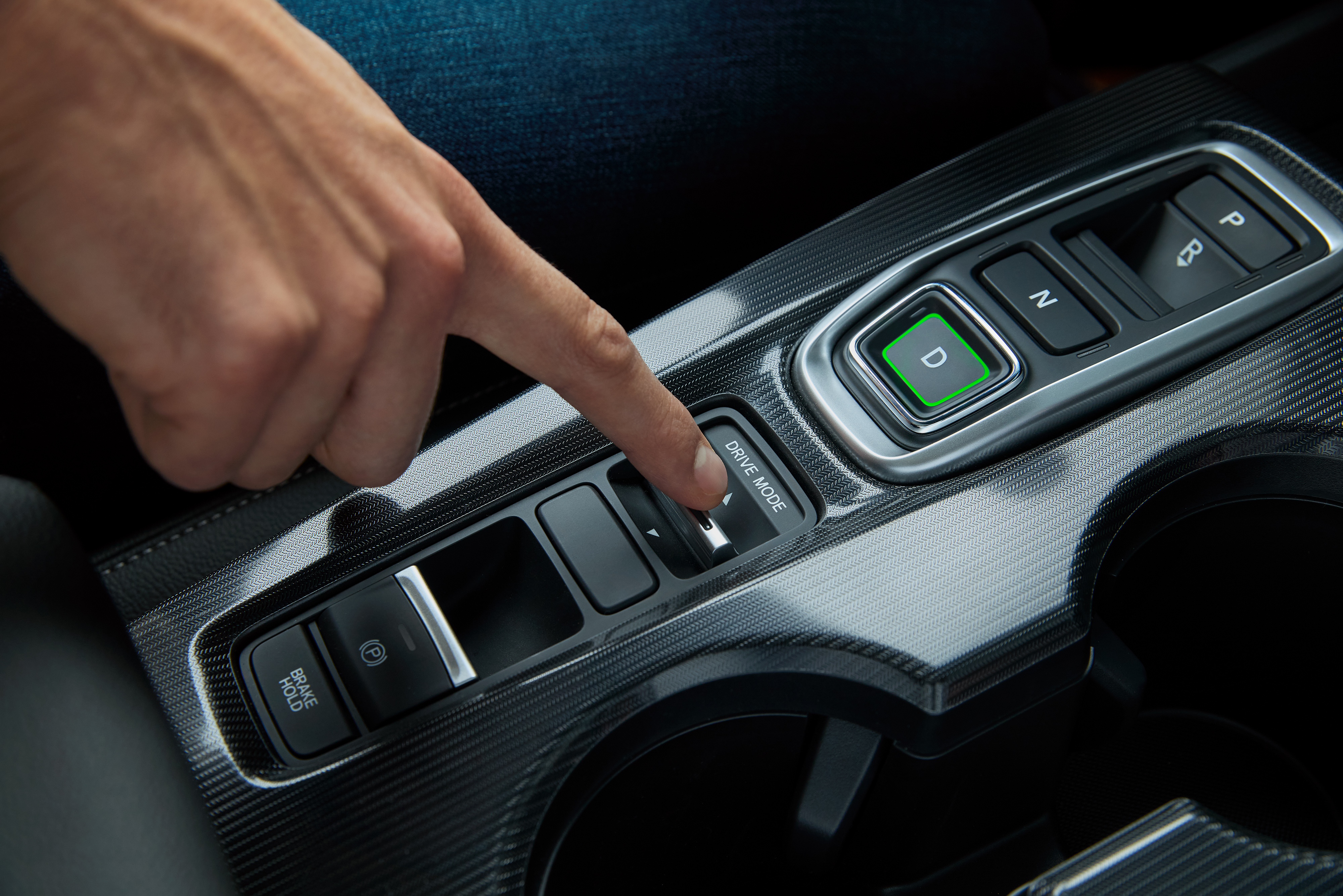 Eine Hand, die den Fahrmodus-Knopf im Inneren eines Honda-Fahrzeugs drücken will