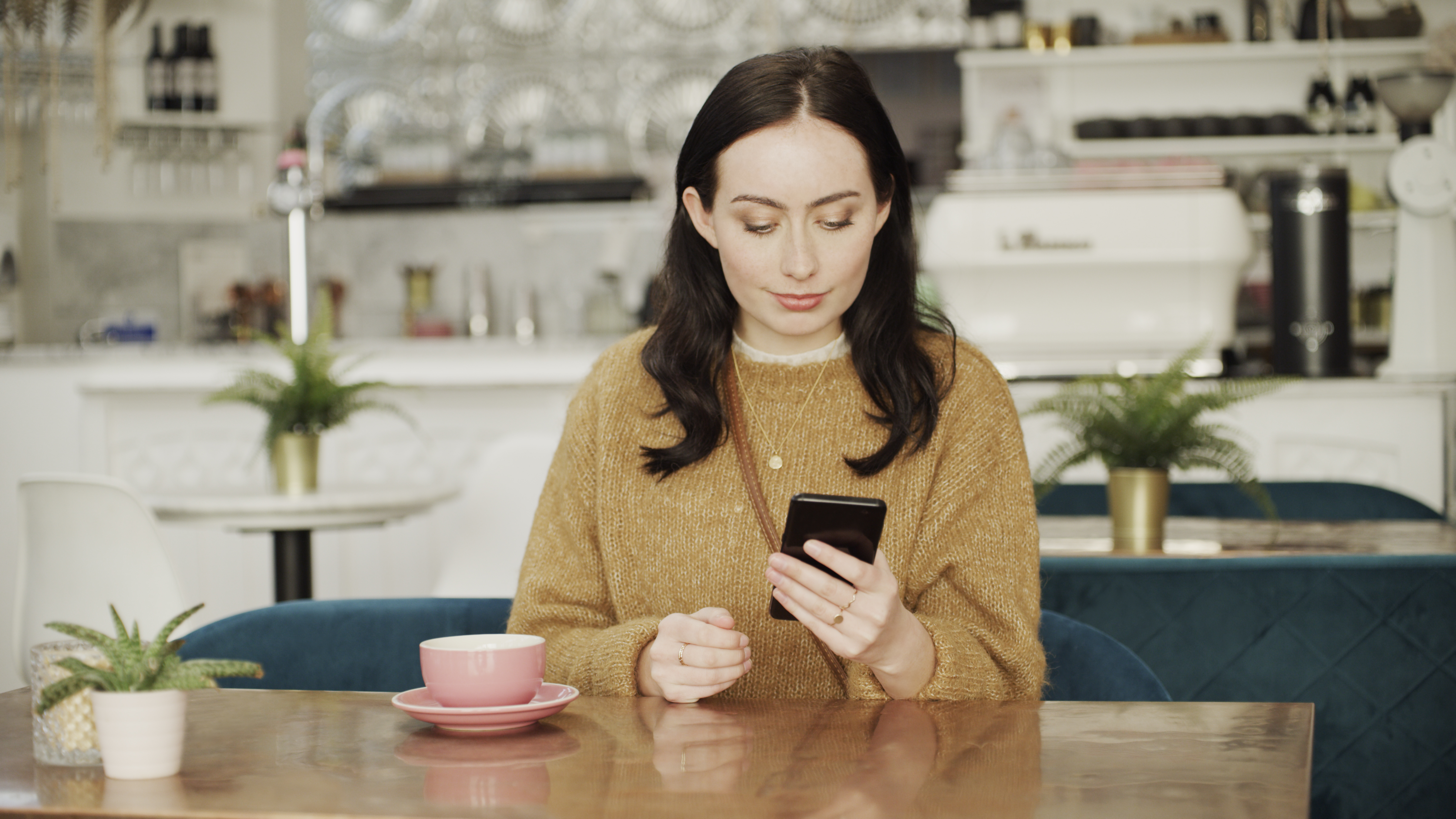 Eine Frau sitzt in einem Cafe und schaut auf ihr Smartphone.
