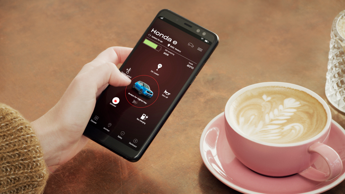 Eine Hand hält ein Smartphone - daneben steht eine Tasse Cappuccino.