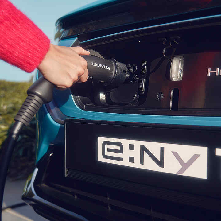 Familie neben einem vor einem Haus geparkten Honda e:Ny1, Frontansicht.