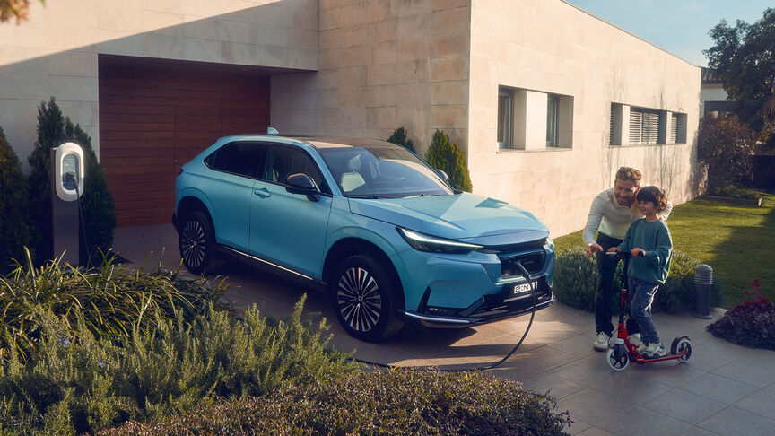 abgewinkelte Ansicht des blauen Honda E Elektroautos, das vom Honda-Ladeger&auml;t aufgeladen wird